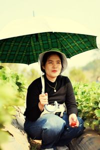 Woman holding umbrella while sitting by plants