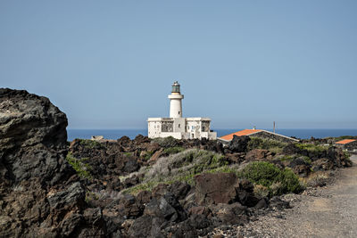 Lighthouse by sea against clear sky