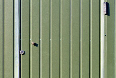 Green metal fence and doors made of corrugated steel sheet  and a surveillance camera.