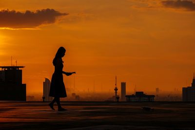 Silhouette woman standing on road against sky during sunset at rooftop 