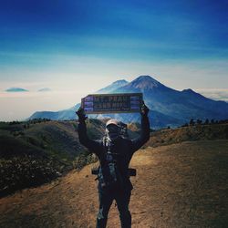 Rear view of man standing on mountain against sky