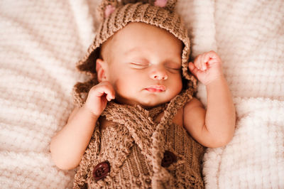 Baby boy sleeping in brown knitted clothing on bed