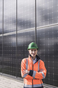 Smiling female engineer with arms crossed standing in front of solar panels
