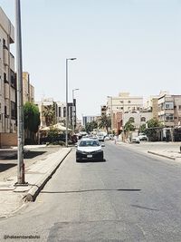 Cars on street by buildings against clear sky