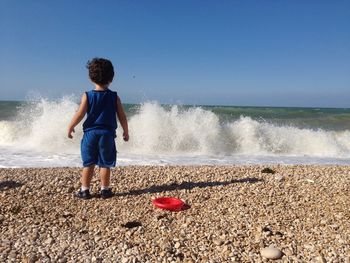 Rear view of boy at beach against clear sky