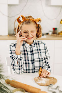 The girl is holding a cookie cutter in her hands, there is dough on the table. 