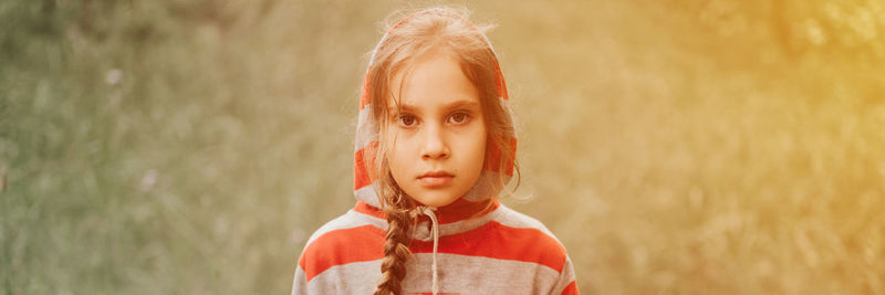 Portrait face of upset or focused thoughtful scowl eight year old kid girl in hood of striped hoodie