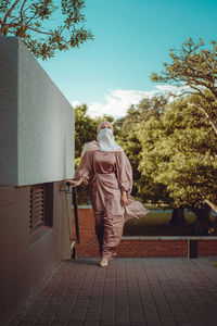 Full length image of veiled woman with white niqab and pink silky dress walking on the path-walk