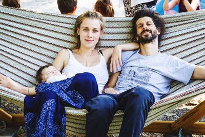 Portrait of parents relaxing with baby on hammock