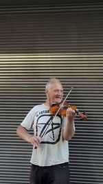 Mature man playing violin while standing against shutter