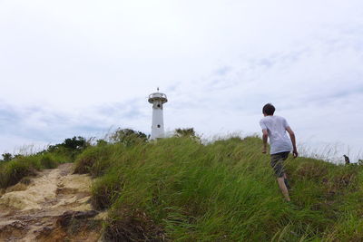 Low angle view of man walking towards lighthouse against cloudy sky