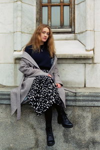 Portrait of young woman sitting on building wall