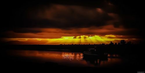 Scenic view of lake against dramatic sky during sunset