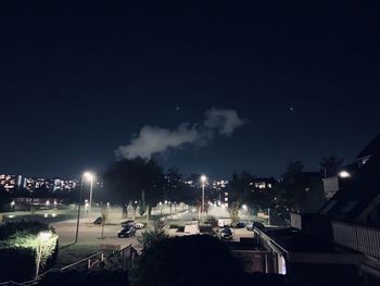 Illuminated street amidst buildings against sky at night