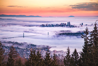 Aerial view cityscape during foggy weather against sky during sunset