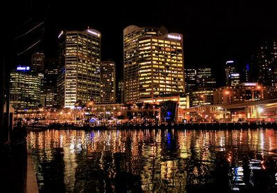 Illuminated buildings by river against sky at night