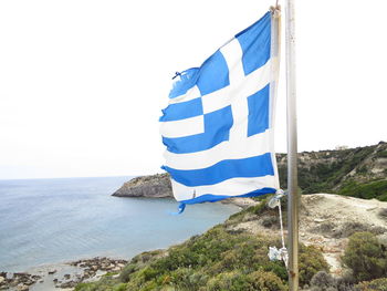 Greek flag waving by sea against clear sky