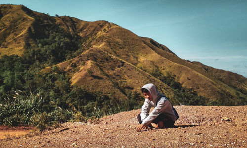 Full length of man sitting on mountain against sky