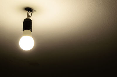 Low angle view of illuminated light bulb hanging on ceiling