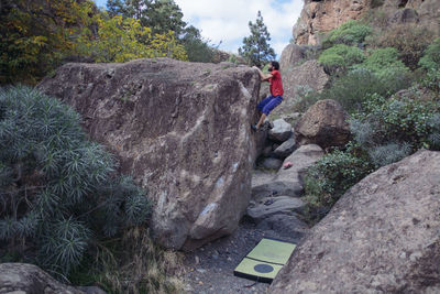 Man climbing on rock formation against sky