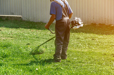 Worker man in protective pants mows the green grass on lawn with autonomous grass mower