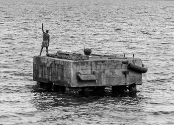 Rear view of man standing on built structure in sea