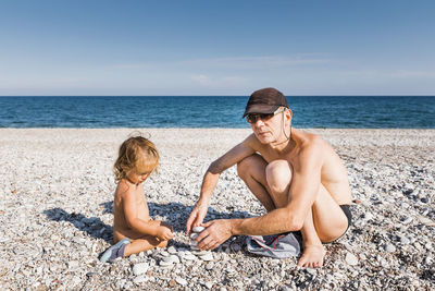 Portrait of shirtless grandfather stacking pebbles with granddaughter at beach