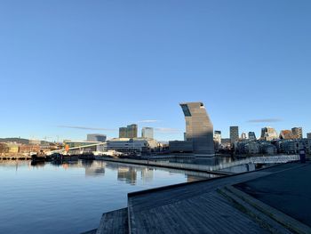 Bridge over river by buildings against clear blue sky