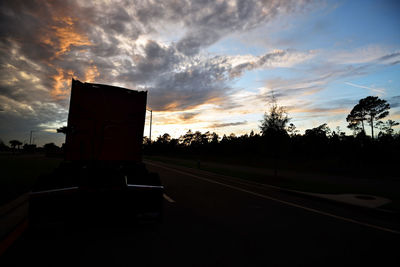 Road by silhouette trees against sky during sunset