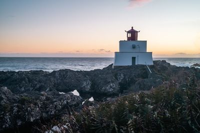 Lighthouse by sea against sky during sunset