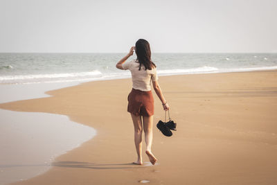Rear view of woman on beach against sky