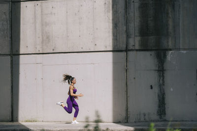 Young woman running on footpath by wall