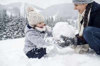 Happy mother with daughter building snowman