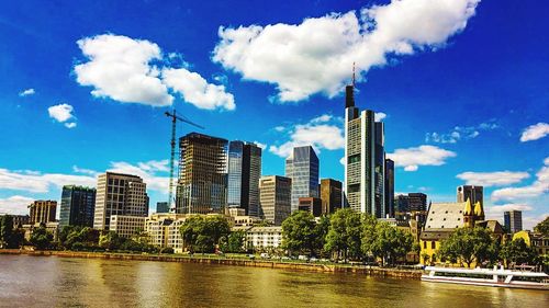 Modern buildings by river against sky in city