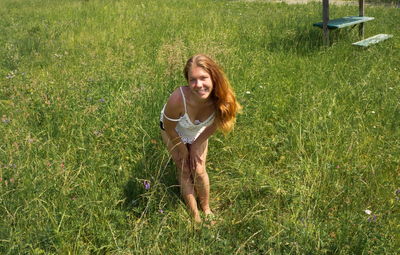 Smiling girl with long red hair stands on a green meadow on a summer sunny day.