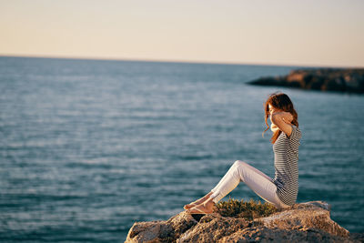 Woman sitting on rock by sea against sky