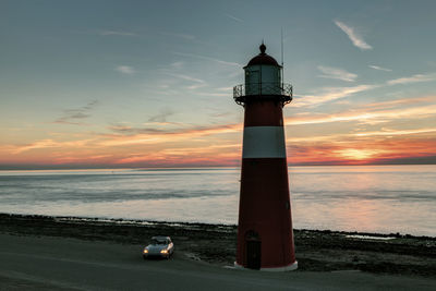 Lighthouse at sea shore against sky during sunset