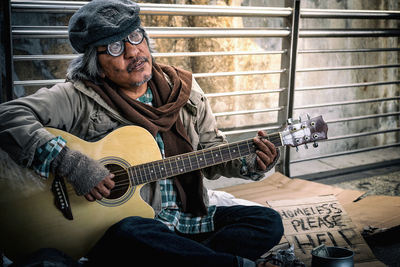 Portrait of homeless man playing guitar while sitting against railing