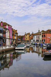 Boats moored in canal by buildings in city against sky
