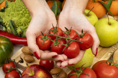 Hands of a girl with red nails holding cherry tomatoes on a table with various types of vegetables