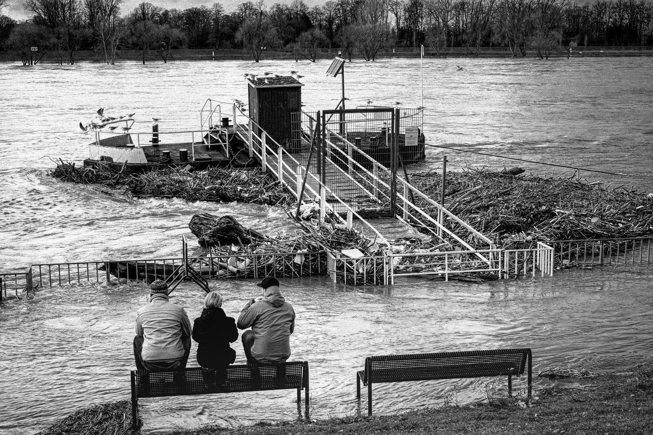 REAR VIEW OF MEN SITTING ON BENCH BY PIER