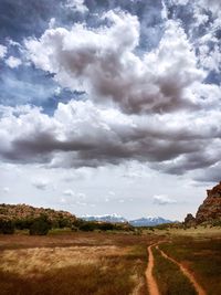 Dirt road amidst field against sky