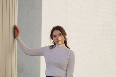 Portrait of young woman standing against wall