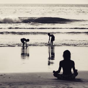 Silhouette men sitting on beach against sky during sunset