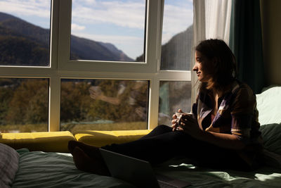 Young woman looking through window at home