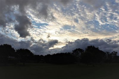 Silhouette trees on landscape against storm clouds