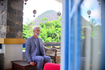 Full length of man in suit sitting on seat against plants