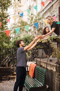 Young woman giving food to smiling male friend from balcony during garden party