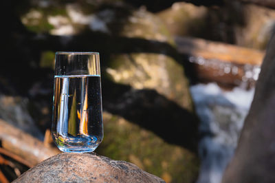 Glass rounded tall glass with drinking clear water stands on a stone in the forest, a fast mountain