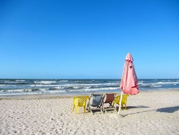Deck chairs on beach against clear blue sky